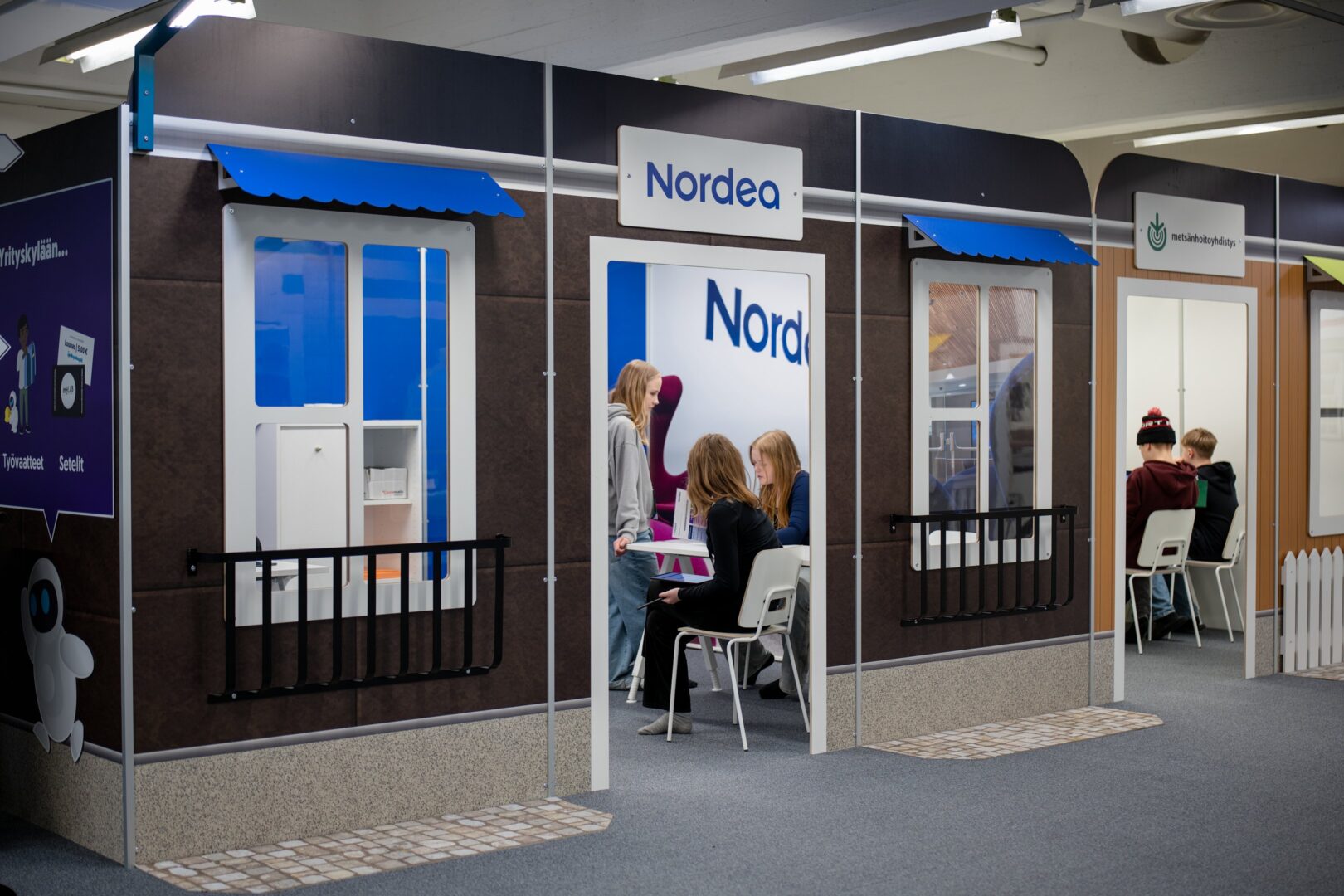 Nuoria istuu pöytien ympärillä Nordean ja Metsänhoityhdistyksen osastoilla Yrityskylässä.