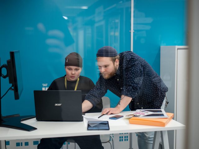 Yrityskylän ohjaaja opastaa kuudesluokkalaista tietokoneella