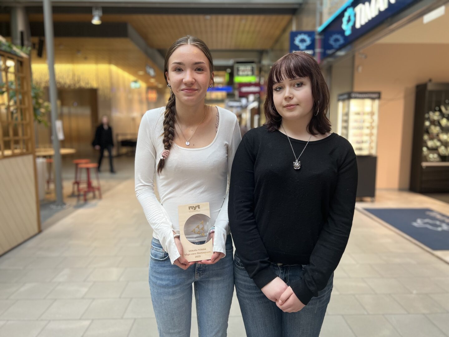 Kaksi nuorta seisoo käytävällä, toisella kädessä palkintopokaali.