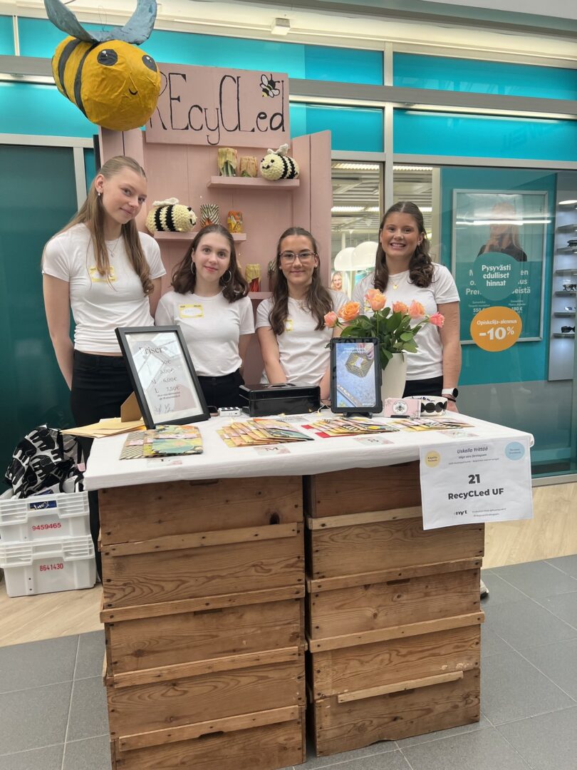 Neljä nuorta seisoo oman messupisteen takana ja hymyilee.