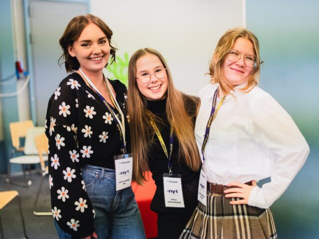 Kolme nuorta hymyilevät kameralle rivissä.