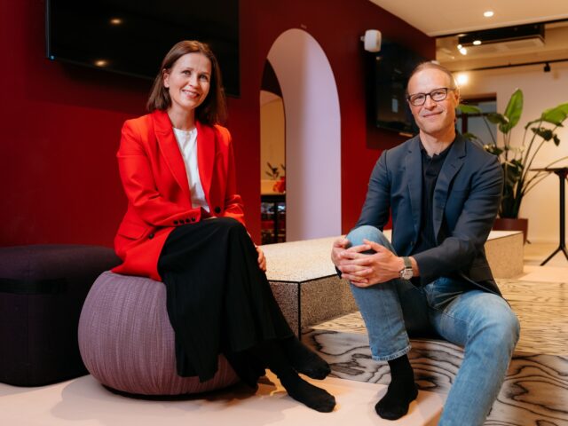 Kaksi henkilöä katsoo kameraan, istuvat korokkeilla lounge-tilassa.