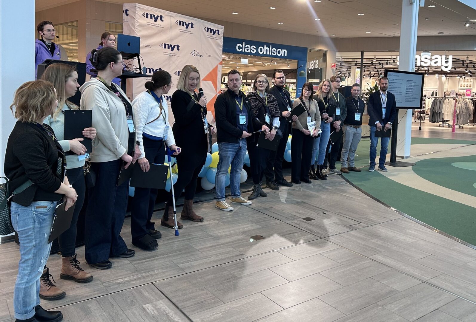 Joukko ihmisiä seisoo ryhmässä tapahtumalavalla.