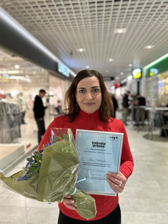 Henkilö seisoo käytävällä kukkakimppu ja diplomi käsissään.