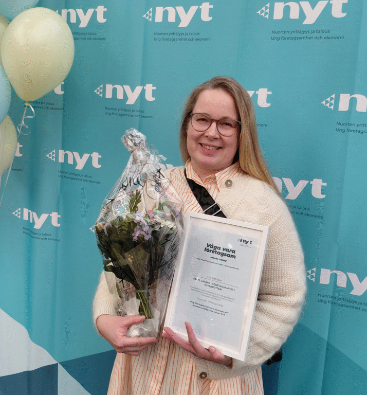 Henkilö kuvausseinän edessä kukkakimppu ja diplomi käsissään.