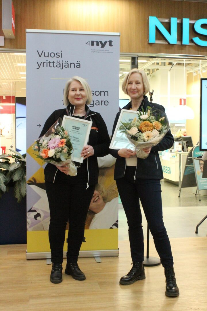 Kaksi naishenkilöä poseeraa kameralle palkintojen kanssa. 