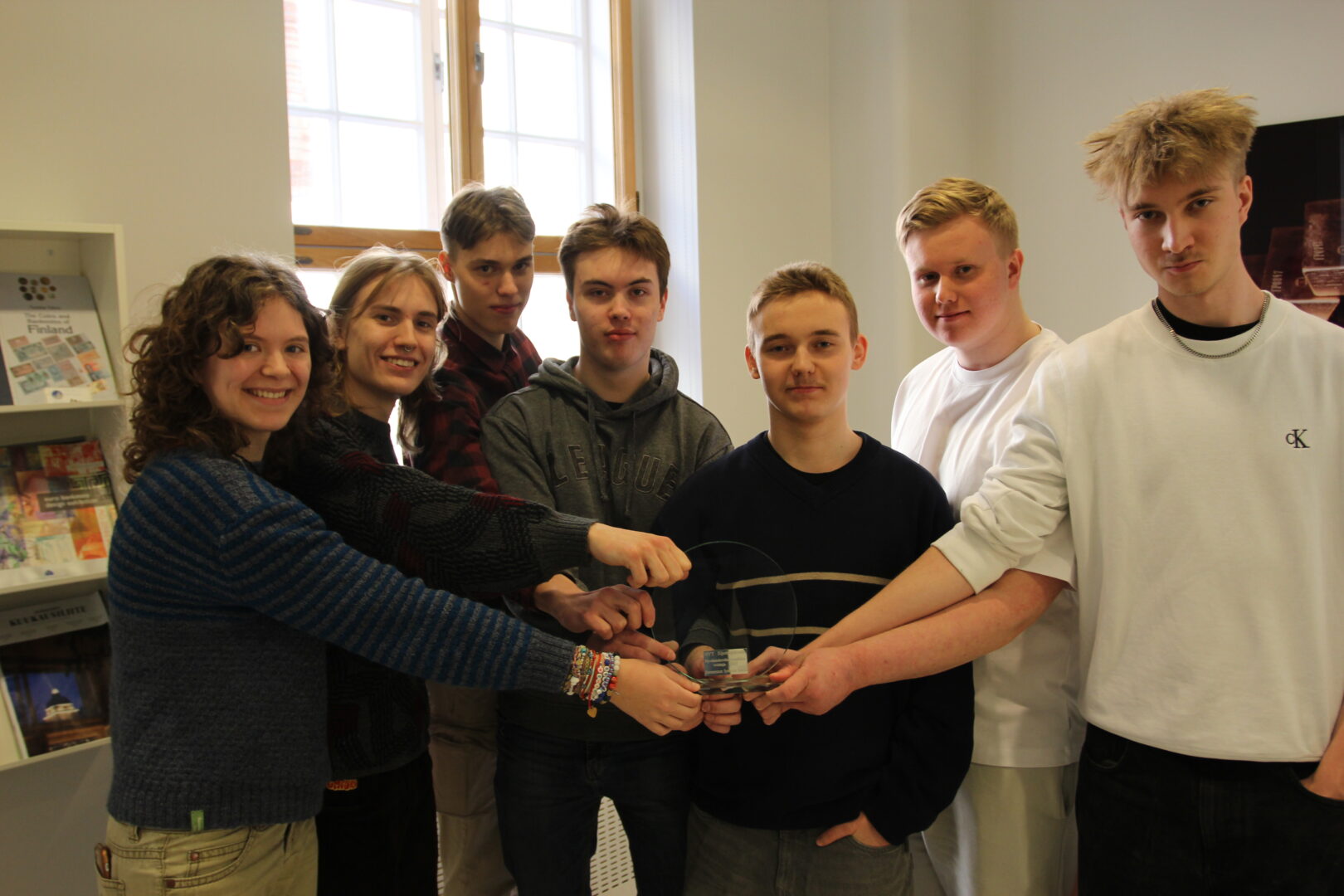 Ryhmä nuoria seisoo vierekkäin ja pitää yhtä kättä kiinni palkintopokaalissa.