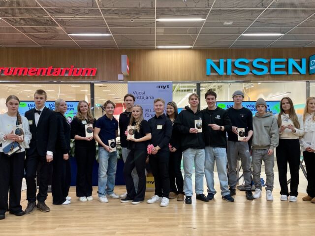 Joukko nuoria seisoo lavalla ja poseeraa kameralle.