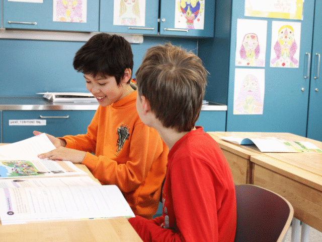 Kaksi lasta istuu pulpettien ääressä ja selaa tehtäväkirjoja.