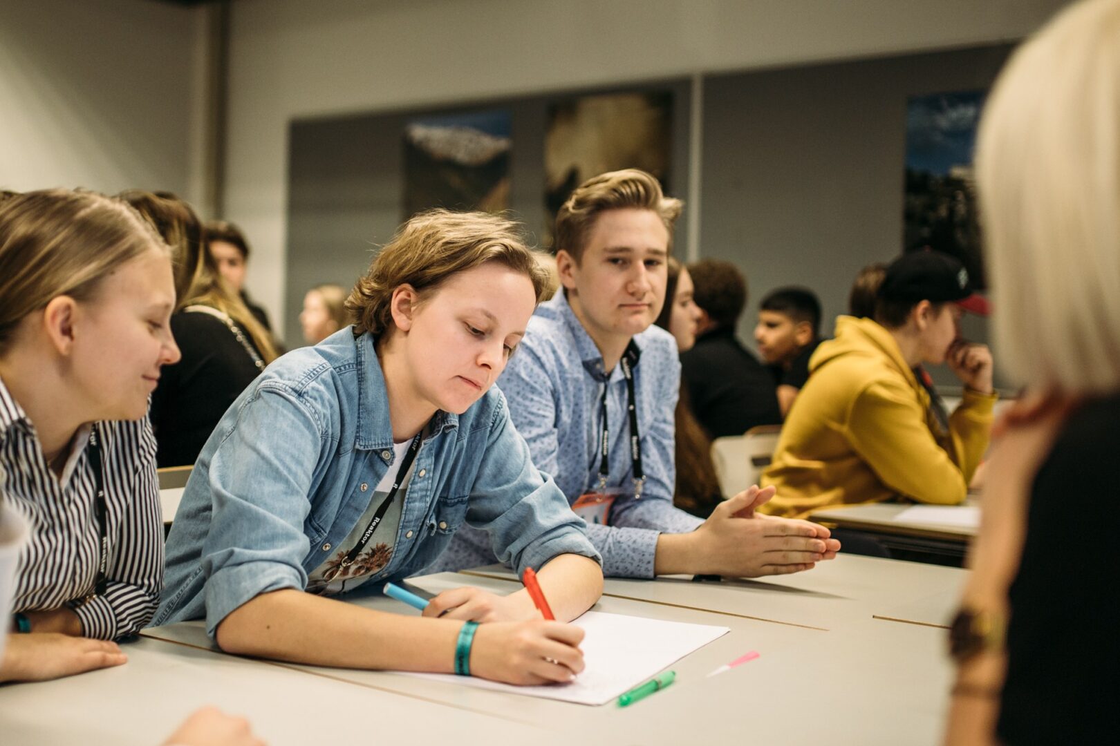 Kolme nuorta pöydän äärellä. Keskimmäinen nuorista kirjoittaa muistiinpanoja